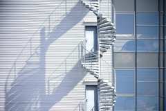 A spiral staircase, fire escape on the side of a industrial building facade.